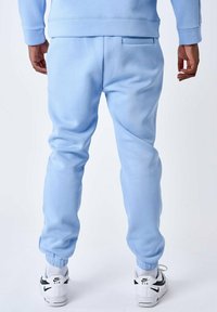 Lichtblauwe joggingbroek van zacht materiaal met elastische boorden en een achterzak, gecombineerd met witte sneakers met zwarte accenten.