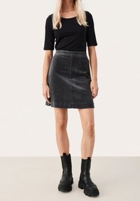Schwarzes ribbesticktes Oberteil, grauer Cordrock mit leichtem A-Linien-Schnitt und strukturiertem Finish. Schwarze Ankle Boots mit dicken Sohlen.