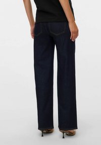 Jeans dritti blu scuro in denim, con tasche posteriori con cuciture a contrasto e vita alta, abbinati a tacchi con motivo.
