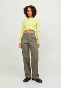 Πράσινο cargo παντελόνι με πλαϊνές τσέπες και χαλαρή εφαρμογή, συνδυασμένο με cropped, μακρυμάνικο, φωσφορίζον κίτρινο τοπ. Μαύρα χοντρά παπούτσια.