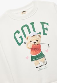Biała bluza z nadrukiem wesołego misia w kolorze pomarańczowym i zielonym, trzymającego kij golfowy, z napisem "GOLF" w wyraźnym zielonym kolorze powyżej.