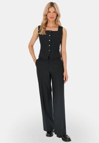 Czarna kamizelka w paski z kwadratowym dekoltem i guzikami z przodu, w połączeniu z szerokimi spodniami. Gładki materiał o dopasowanym kroju.