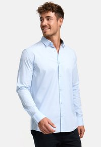 Camisa de manga larga azul claro con cuello abotonado, confeccionada en una tela suave, con un sutil brillo y detalles de cuello en contraste.