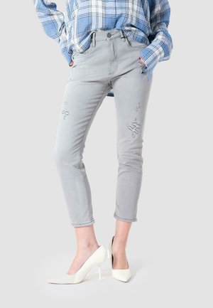 Light gray jeans with a slim fit, featuring distressed detailing. Paired with white pointed-toe heels. Blue plaid shirt draped over.