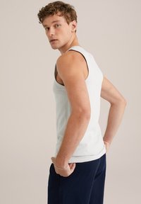 Witte, gestructureerde tanktop met brede schouderbanden, aansluitend ontwerp, zichtbare stiksels en een afgeronde zoom. Getoond op een model van achteren.