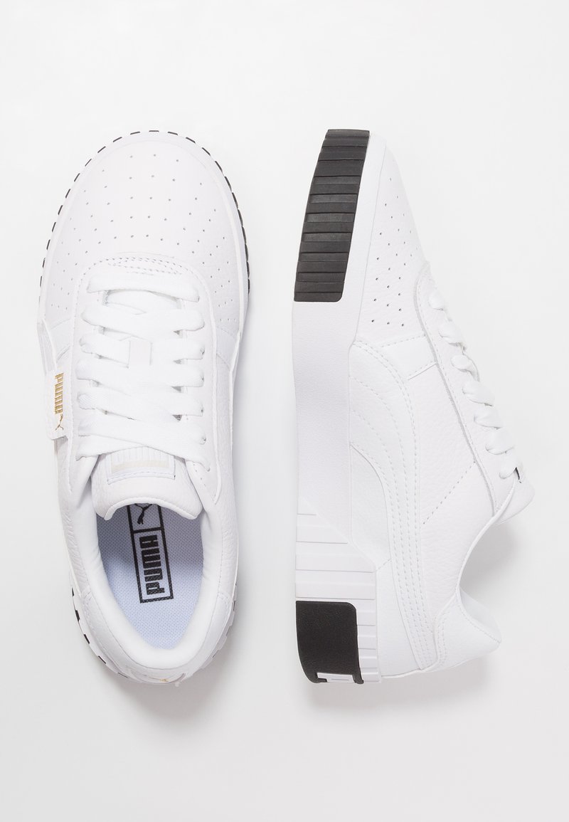 Baskets blanches avec texture perforée, lacets blancs plats et semelle noire à motif. Le côté présente un logo discret et une finition en cuir lisse.