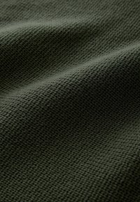 Tissu en tricot vert foncé avec un motif texturé et tissé serré, présentant de légers plis créant des ombres douces.