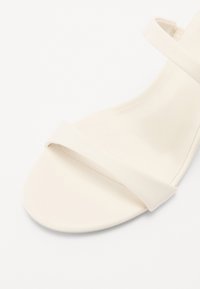 Sandalia plana blanca con un upper de cuero suave y dos correas entrecruzadas. Punta redonda y diseño minimalista, sin hardware o adornos visibles.