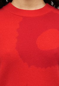 Κόκκινο πουλόβερ πλεκτό με στρογγυλή λαιμόκοψη, με διαβαθμισμένο μοτίβο που μεταβαίνει από πιο σκούρες σε πιο ανοιχτές αποχρώσεις του κόκκινου.