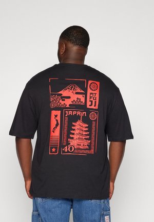 Mies, jolla on musta T-paita, jossa on punainen kuva Fuji-vuoresta, kirsikankukista, pagodasta, Japanin kartasta ja teksti "Japan 40" selässä, siniset farkut.