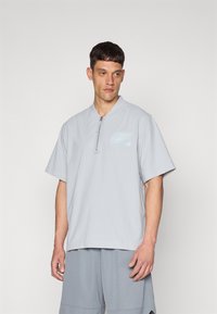 Light gray short-sleeve shirt in breathable material. Features a half-zip closure and a small light blue logo on the left chest.
