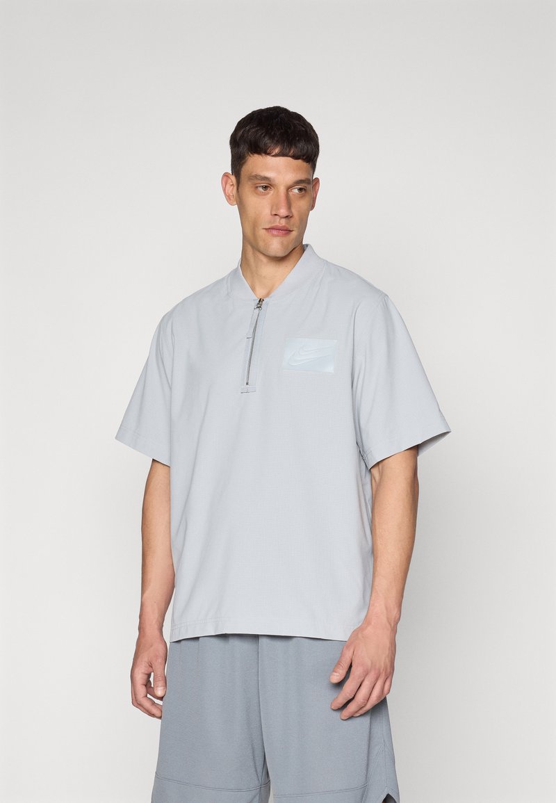 Light gray short-sleeve shirt in breathable material. Features a half-zip closure and a small light blue logo on the left chest.