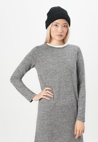 Gray long-sleeve dress with a soft texture, featuring a rounded neckline and a black knitted beanie. Model poses with one hand on hip.