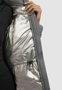Gray padded jacket with a shiny silver lining, featuring quilted texture and a black elastic adjustment loop inside the pocket.