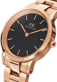 Rose gold metal watch with a black round dial, slim hour markers, and two hands. Features a polished bracelet with a secure clasp.