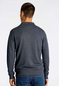 Musta harmaa pitkähiha polo-neule, jossa on ribbineck ja hihansuut, valmistettu teksturoidusta kankaasta, takanäkymä, yhdistetty sinisiin farkkuihin.