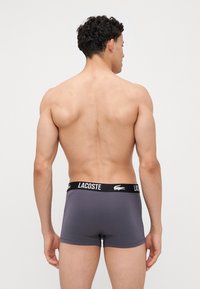 Szürke boxeralsó fekete Lacoste logós derékrésszel, sima textúrával és testhezálló kialakítással. Hátulról nézve.