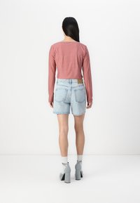 Haut à manches longues à carreaux rouges associé à un short en denim bleu clair, offrant une coupe décontractée. Détails clairs sur les poches arrière, tissu texturé.