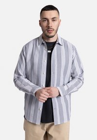 Camisa de botones a rayas en blanco y azul marino, hecha de una tela ligera, con cuello extendido y mangas largas con puños abotonados.