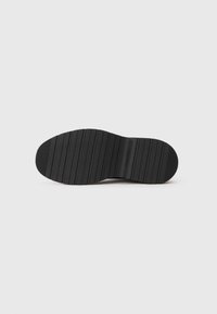 Suela de zapato de goma negra con un patrón de agarre texturizado y un sutil logo, que presenta una forma redondeada y ranuras horizontales para mayor tracción.