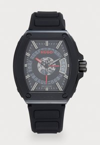 Black rubber strap watch with a rectangular case, transparent back, grey face, white hour markers, red accents, and textured patterns.