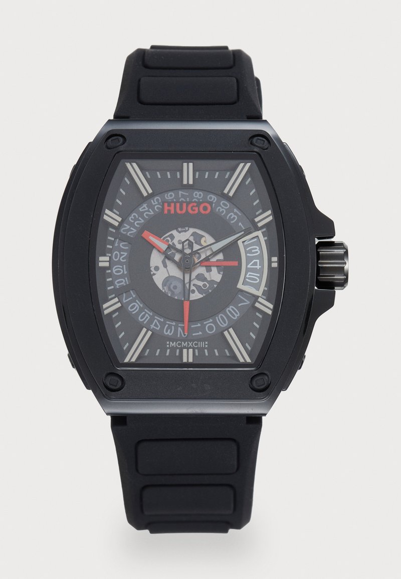 Black rubber strap watch with a rectangular case, transparent back, grey face, white hour markers, red accents, and textured patterns.