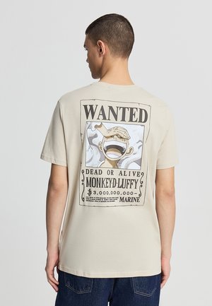T-shirt beige in cotone con grafica in stile fumetto "Wanted" sulla schiena, raffigurante un personaggio con la bocca aperta, circondato da nuvole.