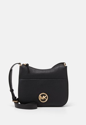 Czarna teksturowana skórzana torebka typu crossbody z regulowanym paskiem i złotym okrągłym logo MK z przodu, zapięcie na zamek u góry.