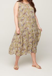 Vestido verde oliva con estampado floral, escote en forma de ojo de llave, diseño sin mangas, cintura fruncida y falda fluida. Llevado con sandalias de tela beige.