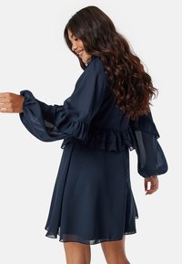 Navy blauwe jurk met geplooide, doorzichtige lange mouwen en een geplooide taille. Vloeiend materiaal, knielang ontwerp, gladde textuur.