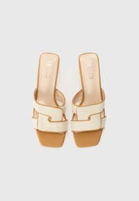 Beige fabric mules with a square toe and crossed straps. Tan sole, embossed logo on the insole. Smooth texture, minimal design.