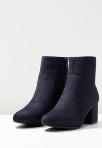 Bottines en daim bleu marine à talon bloc, avec une fermeture éclair latérale et une texture lisse, conçues pour une silhouette ajustée.