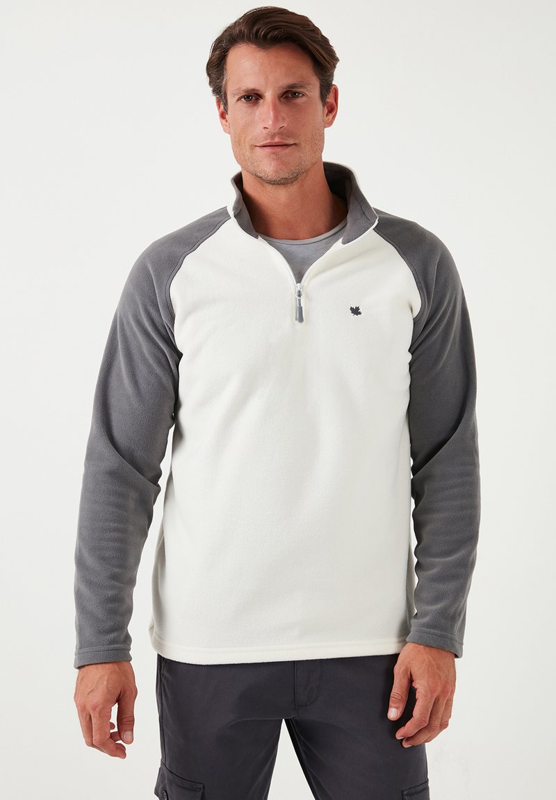 Fleece-pullover med en lynlås krave; cremet krop og grå ærmer; har et lille logo på brystet; blød tekstur.