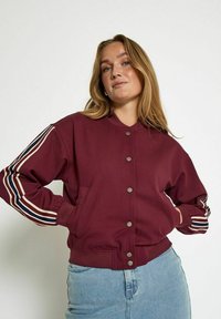 Maroon bomber jacket with a button-up front, contrasting striped sleeves in beige, navy, and white, and side pockets. Soft fabric texture.