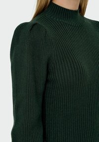 Pull en maille vert foncé avec une texture côtelée, un col montant et des détails d'épaules bouffantes. Design ajusté qui met en valeur les contours.