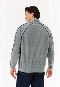 Graue Fleecejacke mit hohem Kragen, schwarzen Akzentnähten an den Schultern und geripptem Saum. Glatte Textur und lockere Passform.