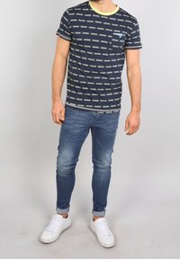 Laivastonsininen t-paita, jossa on vihreät vaakaraitat, pyöreä kaula-aukko ja tasku; yhdistettynä slim fit -vaaleansinihin farkkuihin ja valkoisiin lenkkareihin.