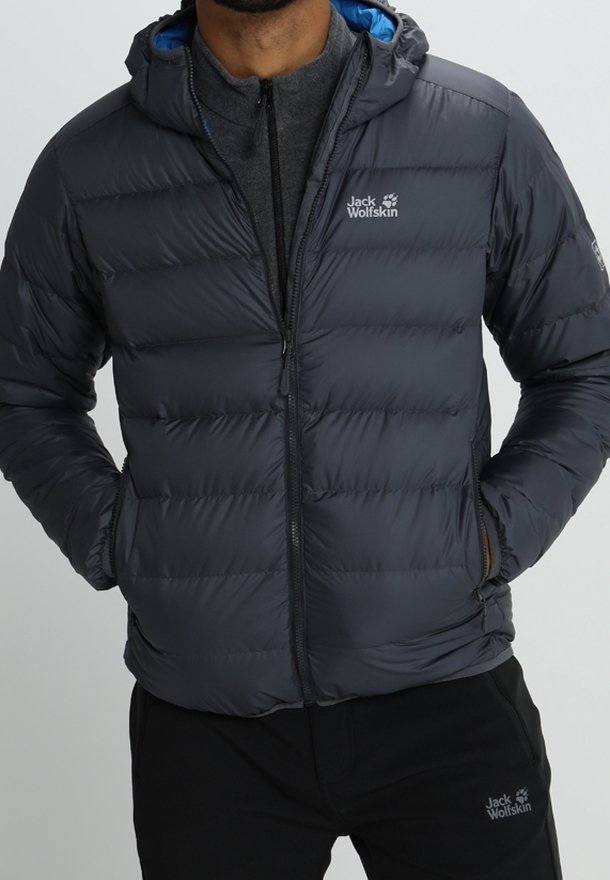 Homme portant une veste matelassée gris foncé de Jack Wolfskin avec les mains dans les poches et un pantalon noir assorti de Jack Wolfskin.