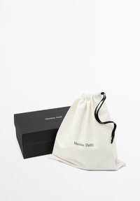 Czarne prostokątne pudełko i biały materiałowy woreczek ze ściągaczem z logo „Massimo Dutti” na białym tle.