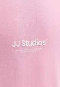 Tissu rose avec le texte blanc "JJ Studios® brought to you by The J&J Crew™ designed in Denmark" centré dessus.