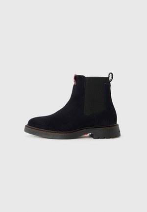 Stivale alla caviglia in suede di un blu navy scuro con pannelli elastici laterali,tracolla e una suola in gomma testurizzata. Presenta cuciture minime e un design classico.