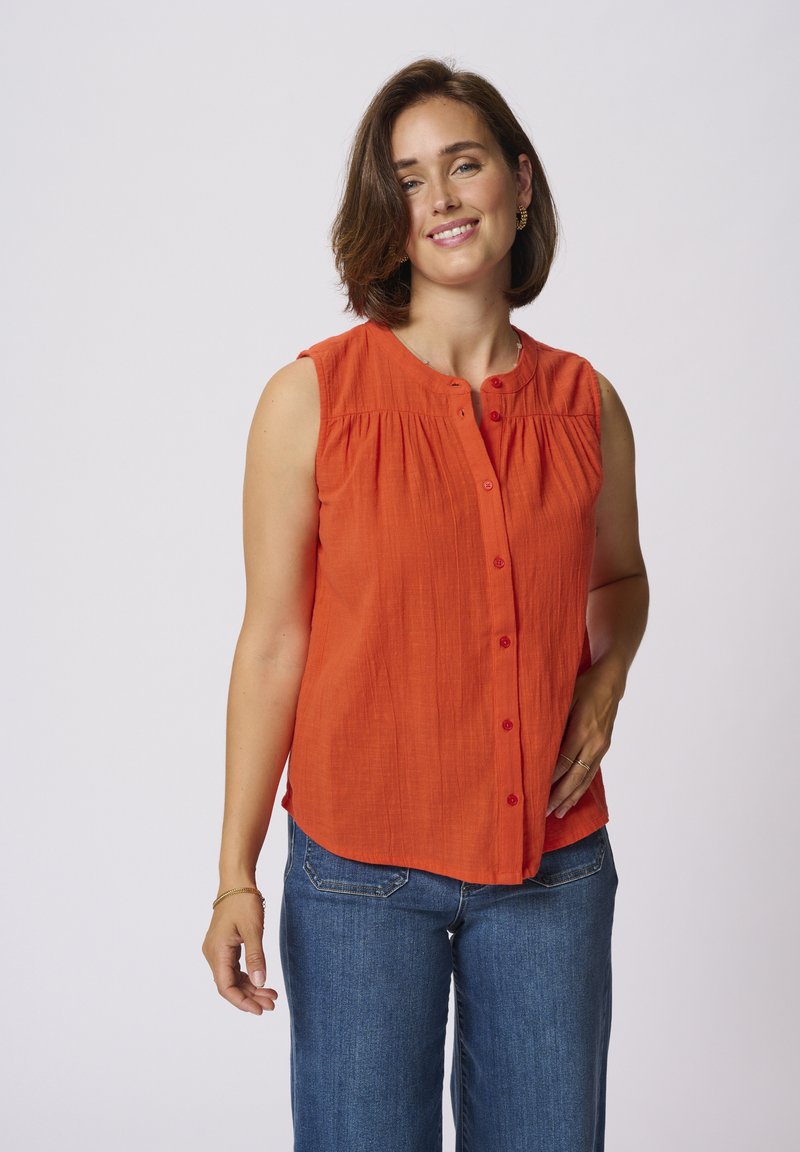 Chemisette sans manches orange avec plis sur le devant, encolure ronde et texture subtile, associée à un jean en denim bleu.