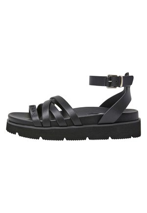 Sort flad sandal med tre frontremme, en ankelrem med sølvspænde, tyk sål og "JEANS" præget på frontremmen.