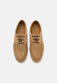 Zapatos de ante marrón con punta redonda, cierre de cordones y costuras tonales. Forro de cuero suave y suela de goma plana. Diseño minimalista.