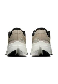 Beige und schwarze Sportschuhe mit einer strukturierten Oberseite, weißer Sohle und schwarzem Gummiprofil. Mit "ON" Branding in Hellgrau.
