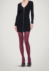 Musta ribbineulottu mekko, jossa etuosassa vetoketju ja kultainen rengas, yhdistettynä burgundinvärisiin kuvioituihin sukkahousuihin ja mustiin korotettuihin korkokenkiin.