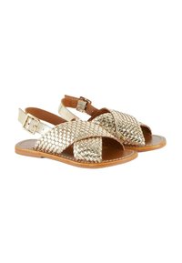 Sandales en or tressé avec un design à bretelles croisées, dotées d'une fermeture par boucle et d'une semelle en cuir beige, mettant en valeur une surface texturée et brillante.