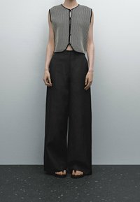 Svarta vida byxor i kombination med en ärmlös, randig stickad topp med knappframtill och en rundad nederkant.