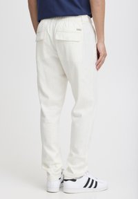 Witte linnen broek met een elastische tailleband, twee achterzakken en een relaxte pasvorm, gecombineerd met klassieke witte sneakers met zwarte strepen.
