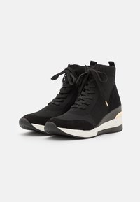 Zapatillas altas negras con una mezcla de materiales textiles y de ante, con una suela cuña blanca y un acento dorado en el talón.
